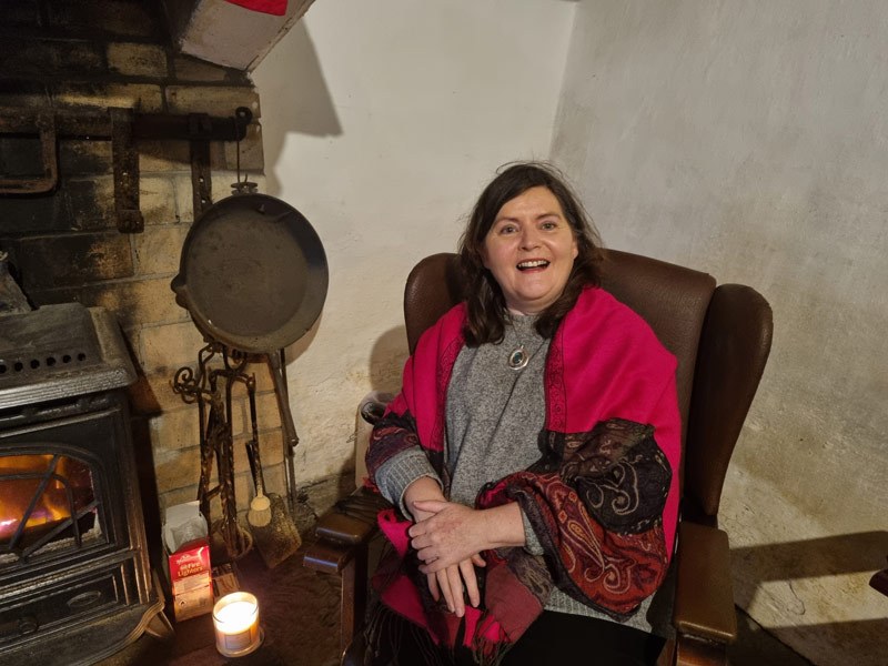 Maria Gillen sitting by fire smiling